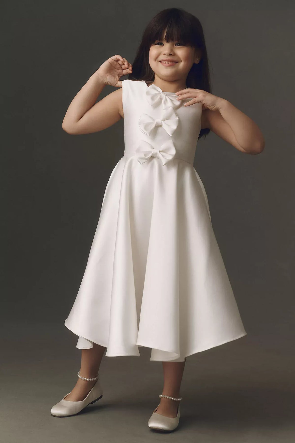 Heowos white flower girl dress with three front bows, a round neckline, sleeveless bodice and tea-length A-line skirt.