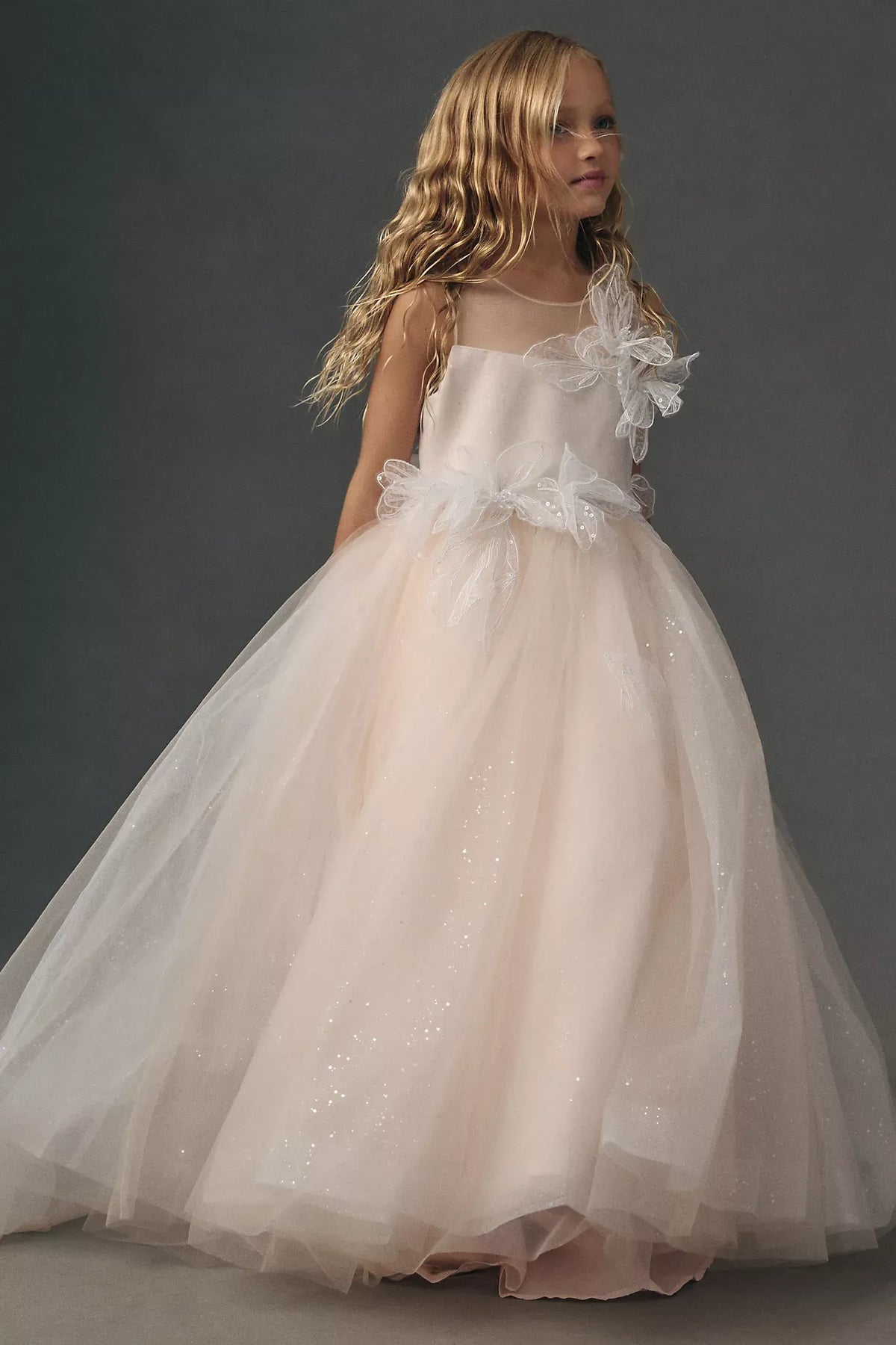 Heowos blush pink flower girl ballgown with an illusion neckline, sleeveless bodice, 3D floral accents and sparkling tulle skirt.